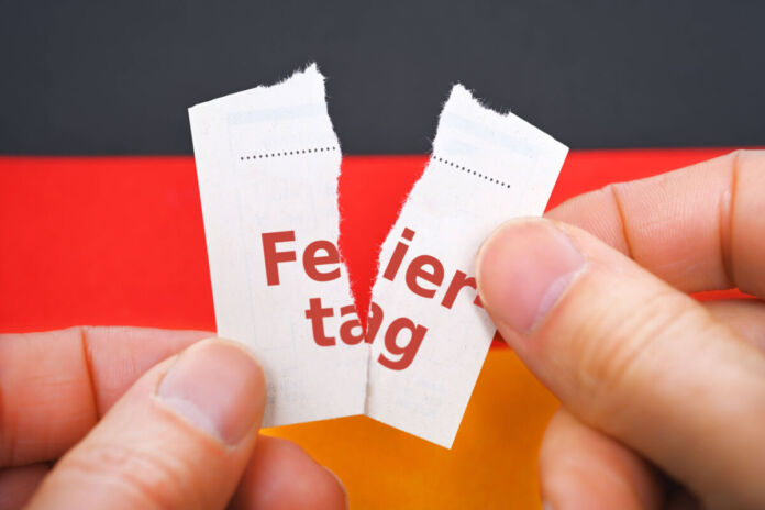 Das Bild zeigt zwei Hände, die ein Papier mittig zerreißen. Auf dem Papier steht in roter Schrift das Wort "Feiertag", das durch das Zerreißen in zwei Teile getrennt ist.