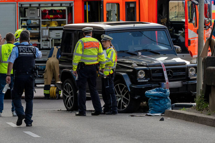 Eine schwarze G-Klasse von Mercedes ohne Fahrer steht auf einer Straße. Um den Geländewagen stehen mehrere Polizisten. Hinter dem Auto steht ein Feuerwehrwagen.