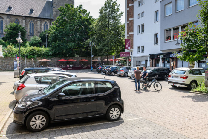 Ein öffentlicher Parkplatz in einer deutschen Innenstadt. Viele Wagen haben hier geparkt. Im Hintergrund ein Fahrradfahrer, Häuser mit einem Geschäft. Ein berühmter Platz in Karlsruhe soll autofrei werden.