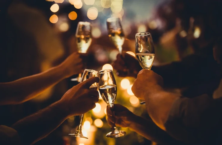 Silvester Sekt Champagner Alkohol Getränk Gläser Promille Feier Neujahr anstoßen Mehrere Personen, deren Arme und Hände zu sehen sind, stoßen mit einem alkoholischen Getränk in Sektgläsern an. Im Hintergrund erzeugen Lichterketten oder Kerzen eine warme, feierliche Atmosphäre.