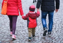 Auf dem Bild sind zwei Erwachsene und ein Kind zu sehen. Das Kind läuft zwischen den beiden Erwachsenen, die es jeweils an einer Hand halten.